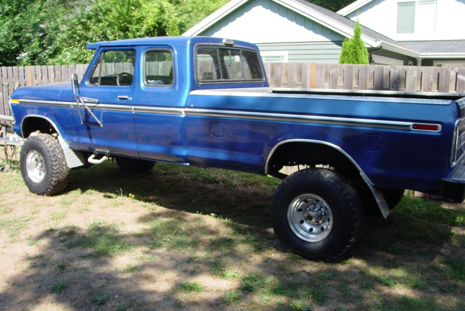 Blue lifted Ford extended-cab long-bed pickup parked in a yard, side view