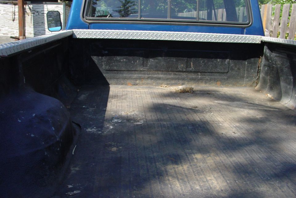 Blue Ford pickup bed with black drop-in liner and diamond plate rail caps