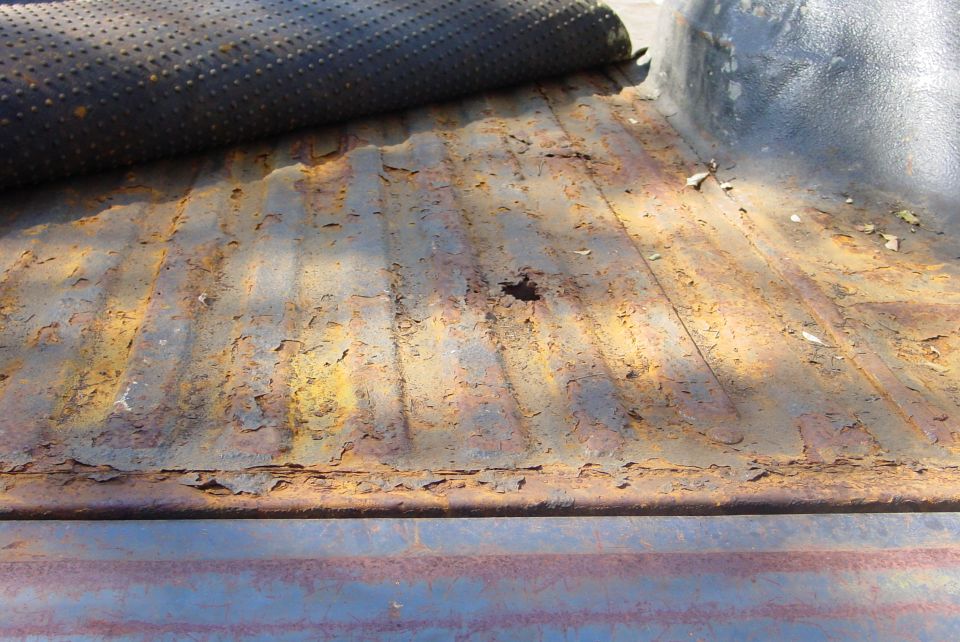 Rusted ribbed truck bed floor with peeling paint and a rust hole