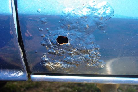 1993 Ford Bronco - Severe rust damage with a hole has formed on the lower section of a blue vehicle's door panel.