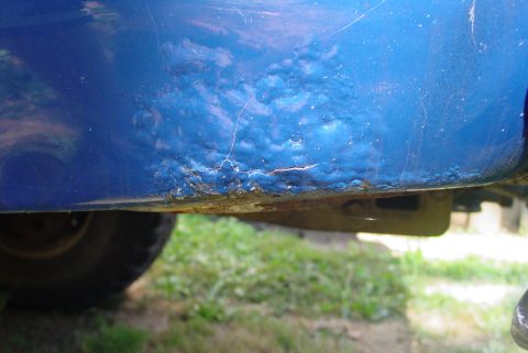 1993 Ford Bronco - This close-up shows significant rust and paint bubbling on the lower body panel of a blue vehicle.