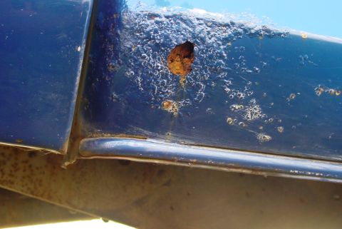 1993 Ford Bronco - Close-up of rust damage on a blue vehicle's body panel, showing a hole and corroded paint.