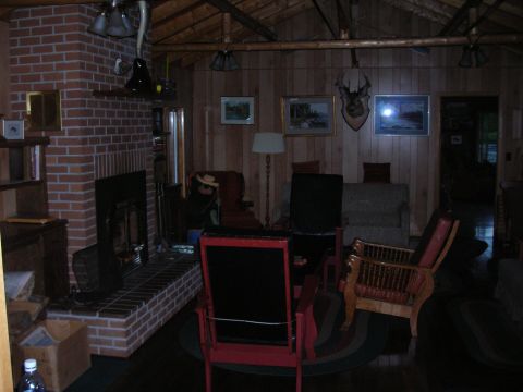 1984 Ford Bronco - A dimly lit room with a large brick fireplace and wooden walls, furnished with chairs and a lamp.