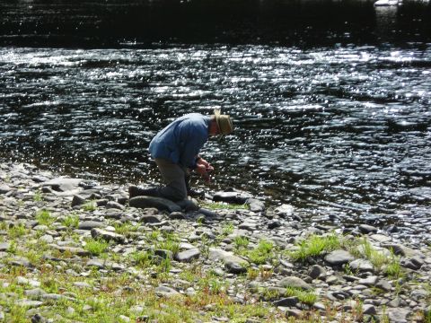 1984 Ford Bronco - A man kneels by the edge of a sparkling river, with a watermark visible in the lower right corner.