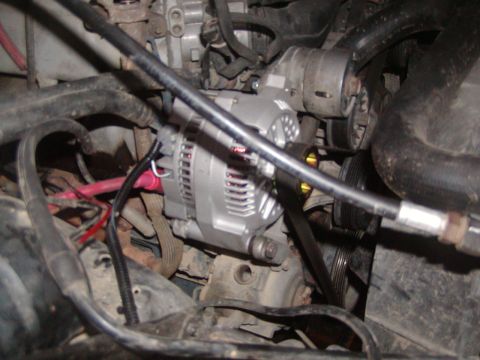 1991 Ford Bronco - Engine bay view of a newly installed alternator with a clean silver case and red positive lead, mounted low on the passenger side and drive…