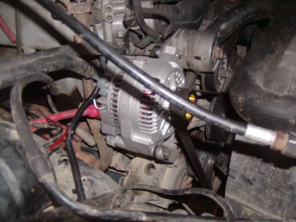 New silver alternator installed in an engine bay with serpentine belt and red lead