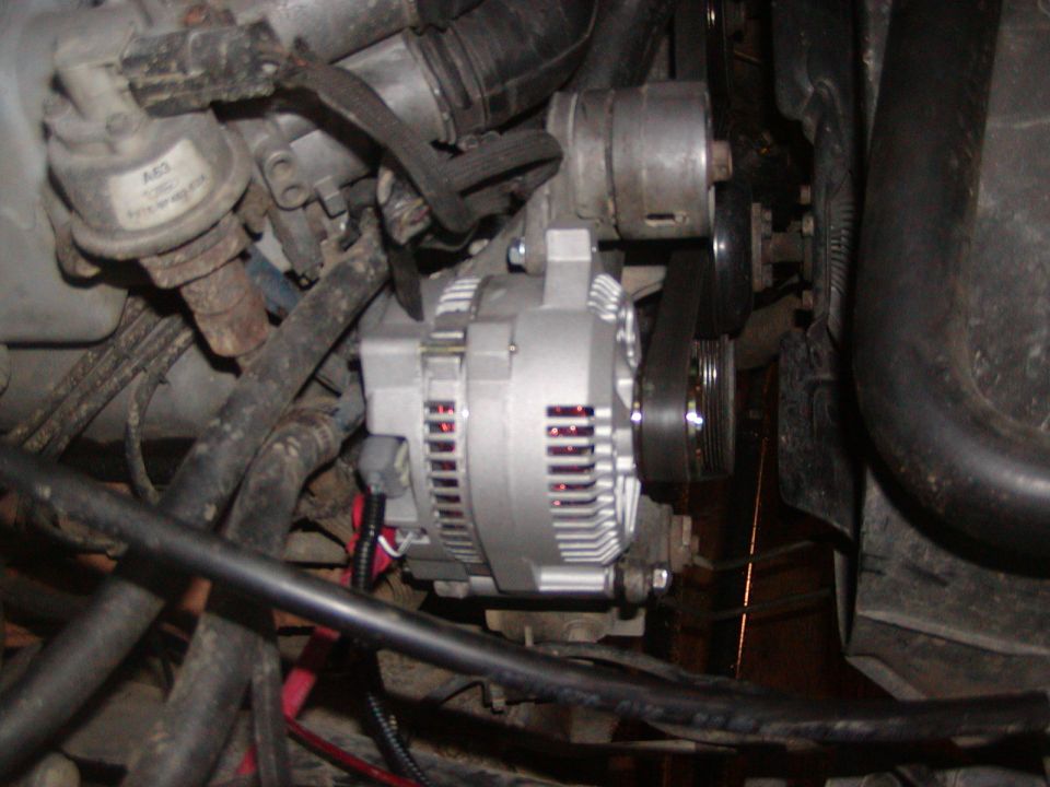 Close-up of a vehicle's engine bay showing an alternator, belts, hoses, and other engine parts