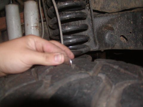 1991 Ford Bronco - Close-up of vehicle suspension components and tire tread, with a hand holding a coin for scale.