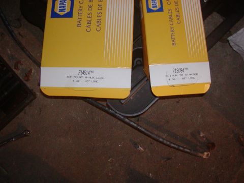 1991 Ford Bronco - Two yellow NAPA battery cable boxes on a shop floor, labeled 714514 'Top Mount w/ Aux Lead, 4 GA - 45" long' and 716094 'Switch to Starter,…