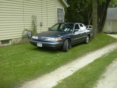 1996 Ford Crown Victoria - Sedan parked on lawn beside a house, with a dirt driveway to the right.