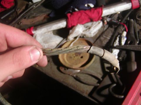 1991 Ford Bronco - A hand holds up a badly corroded battery or charging cable with cracked, oil-soaked insulation and a taped repair near the terminal end. Be…