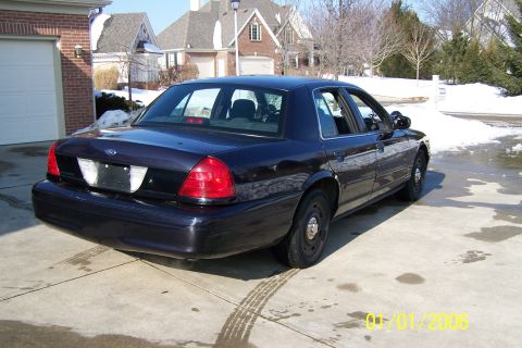 2003 Ford Crown Victoria - A dark blue 2003 Ford Crown Victoria sedan is viewed from the rear on a sunny day with snow in the background.