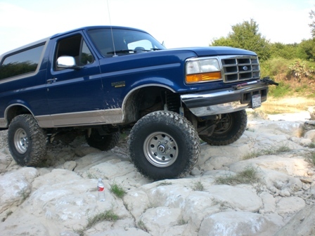 1996 Ford Bronco - A blue 1996 Ford Bronco navigates a rocky trail with large off-road tires.