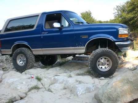 1996 Ford Bronco - A blue 1996 Ford Bronco navigates a rocky obstacle course, its off-road capabilities.