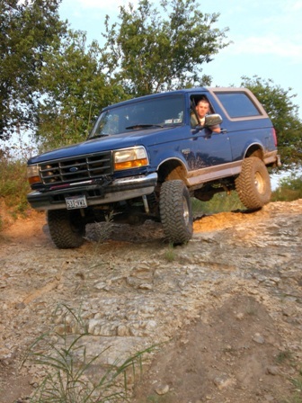 1996 Ford Bronco - A blue 1996 Ford Bronco navigates a challenging off-road course with a driver visible behind the wheel.
