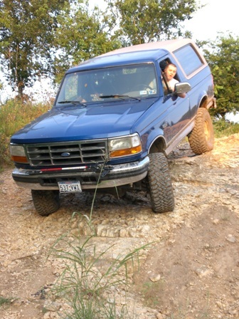 1996 Ford Bronco - Blue 1996 Ford Bronco navigating a rough, off-road path with a person in the driver's seat.