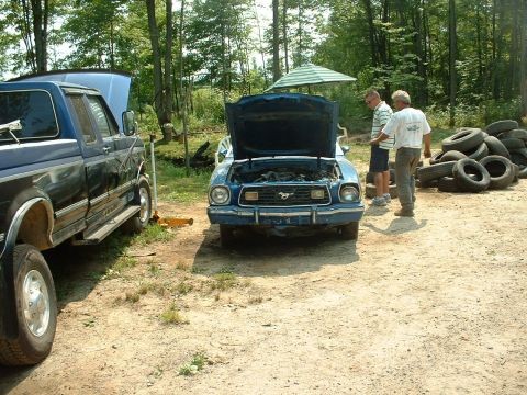 1978 Ford Mustang II - A blue Ford Mustang II sits with its hood open, next to a blue pickup truck, with two men nearby.