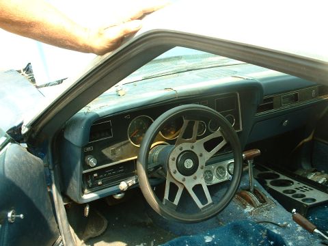 1978 Ford Mustang II - The interior of a 1978 Ford Mustang II shows wear and tear, with an aftermarket steering wheel and blue carpeting.