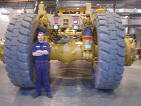 1966 International School Bus - A person stands next to the massive rear axle and wheels of a yellow mining truck, providing a sense of scale.