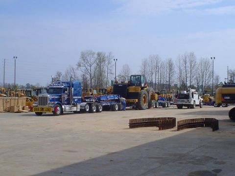 1966 International School Bus - A blue semi-truck is parked next to a large yellow construction vehicle, with more equipment in the background.