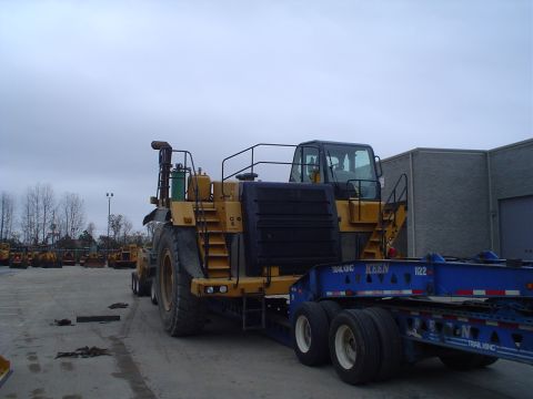1966 International School Bus - A large yellow hauler is loaded onto a blue trailer, parked in an outdoor lot.