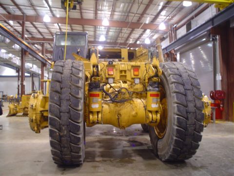 1966 International School Bus - Rear view of yellow heavy machinery with large tires and visible hydraulic systems inside a workshop.