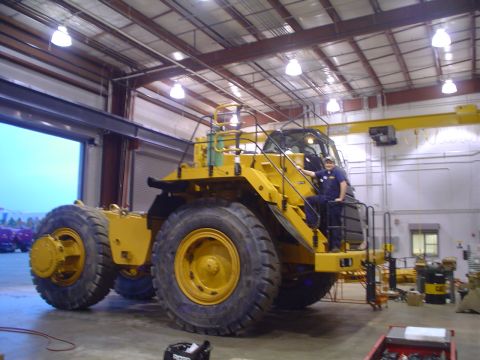 1966 International School Bus - A large yellow articulated dump truck is parked inside a building, with a person standing on its access steps.