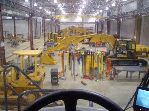 1966 International School Bus - Multiple yellow construction vehicles are parked inside a large workshop with overhead lighting.