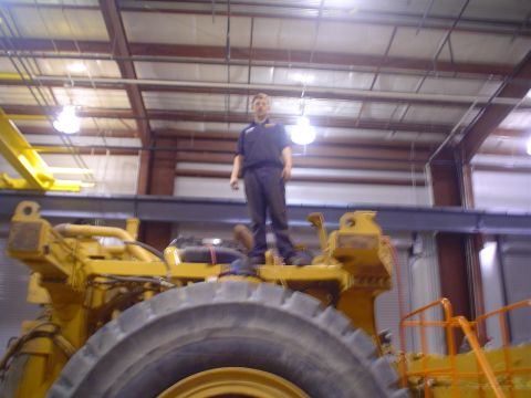 1966 International School Bus - A person stands atop a large piece of yellow heavy machinery inside a warehouse.