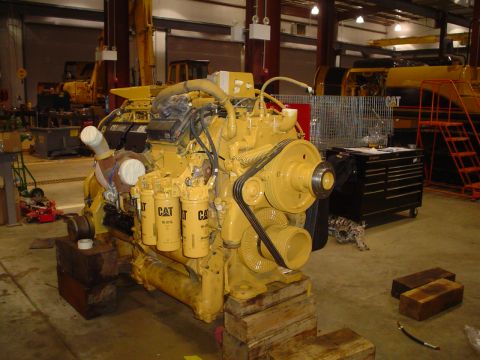 1966 International School Bus - A large yellow Caterpillar engine is displayed on wooden blocks in a workshop setting.