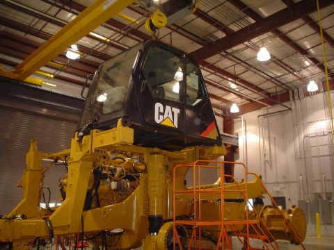 1966 International School Bus - A CAT heavy machinery cab is lifted by a crane inside a workshop.