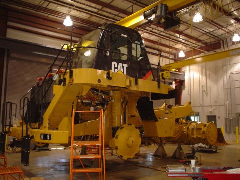 1966 International School Bus - Heavy machinery, a Caterpillar mining truck, is suspended and undergoing maintenance in a large workshop.