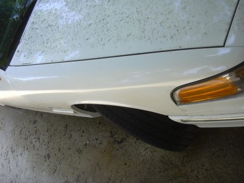 1997 Ford Crown Victoria - Close-up view of the front fender, headlight, and tire of a white sedan.