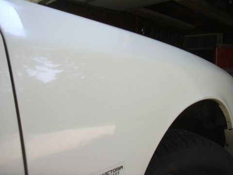 1997 Ford Crown Victoria - Close-up of a white car's fender, showing a portion of the wheel well and a small badge.