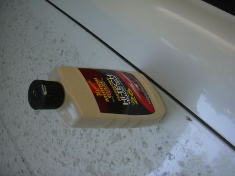 1997 Ford Crown Victoria - A bottle of car wax rests on a soiled white surface, with a black trim line visible.