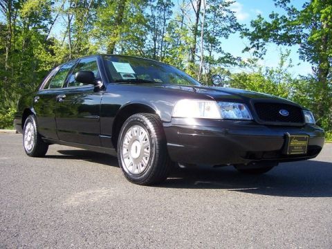 2003 Ford Crown Victoria - A black 2003 Ford Crown Victoria sedan is parked on an asphalt surface with trees in the background.