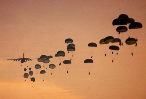 1990 Ford Bronco - An airplane deploys paratroopers during a jump, with many parachutes visible against the sunset sky.