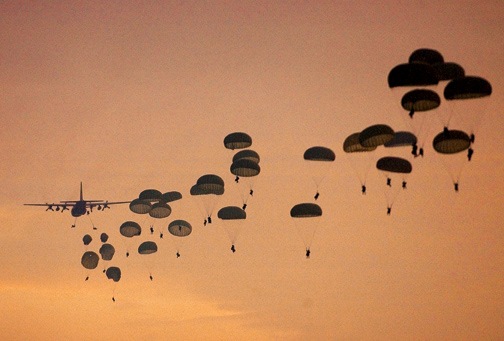 Airplane dropping paratroopers against an orange sky