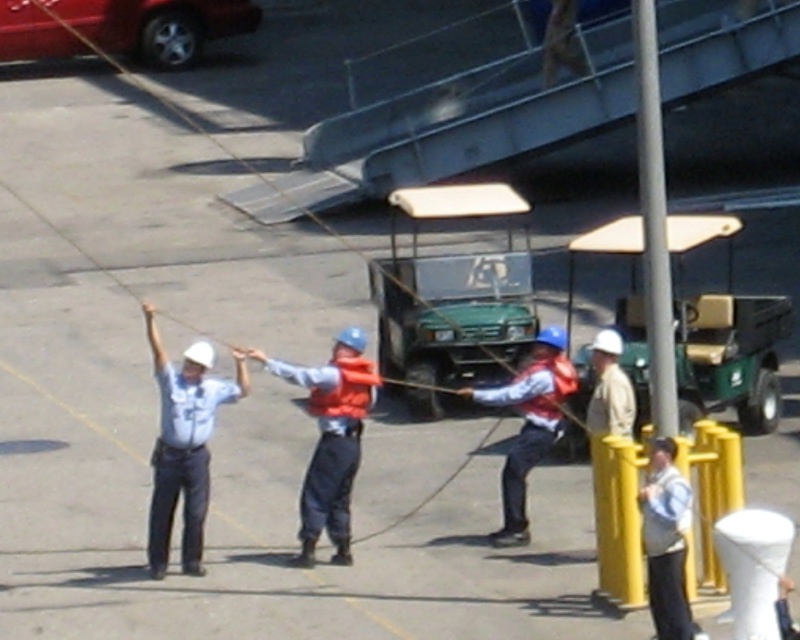 Workers in hard hats and life vests handling a mooring line on a dock