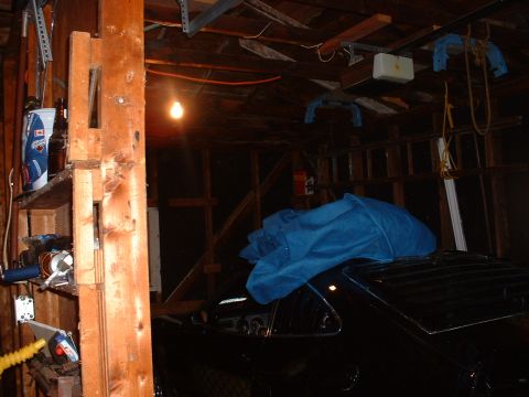 1978 Ford Mustang II - A black 1978 Ford Mustang II coupe is partially covered by a blue tarp inside a cluttered garage.
