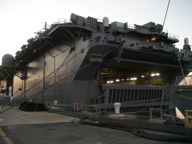 Large gray amphibious assault ship moored at a pier at dusk