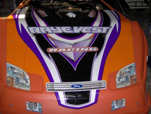 1978 Ford Bronco - Front view of an orange racing car with "RAYGVEST RACING" graphics and a Ford emblem.