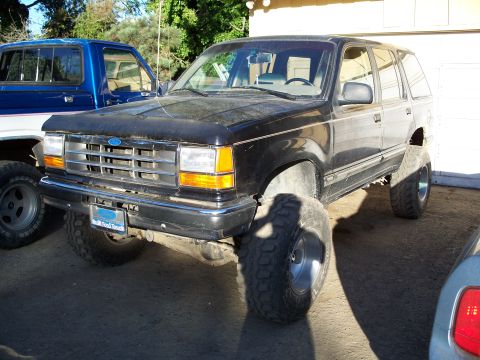 1990 Ford Bronco - A modified black Ford Explorer SUV is shown from the front-three-quarter view, parked outdoors.