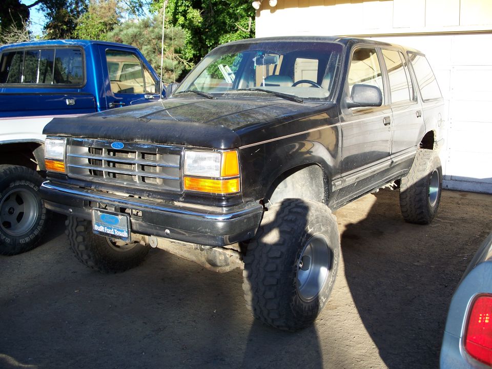 Black Ford Explorer SUV with lifted suspension and large tires, parked next to a blue pickup truck
