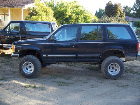 1990 Ford Bronco - A black SUV is parked outdoors, lifted with large off-road tires, with another vehicle visible behind it.