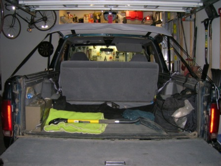 1995 Ford Bronco - The cargo area of a 1995 Ford Bronco is visible, with tools and bags stored inside. A bicycle hangs on the wall of the garage.