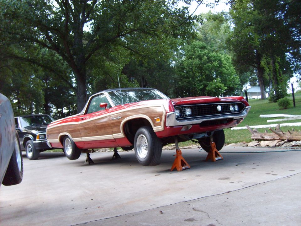 Red and wood-paneled 1970 Ford Ranchero on orange jack stands, front end raised