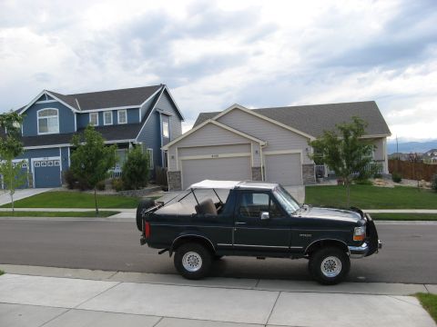1995 Ford Bronco - A dark green Ford Bronco is parked on a suburban street in front of two houses.