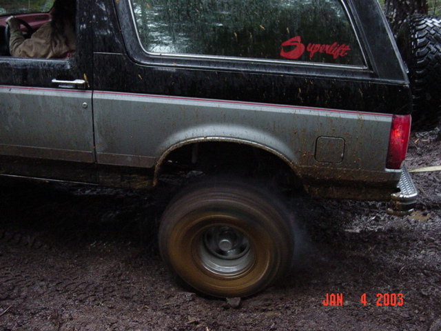 Close side shot of dark Bronco with Superlift decal spinning a muddy rear tire