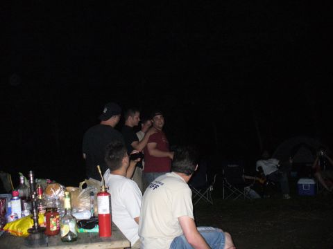 1991 Ford Probe - A group of people are gathered at a campsite at night, with drinks and food laid out on a table.